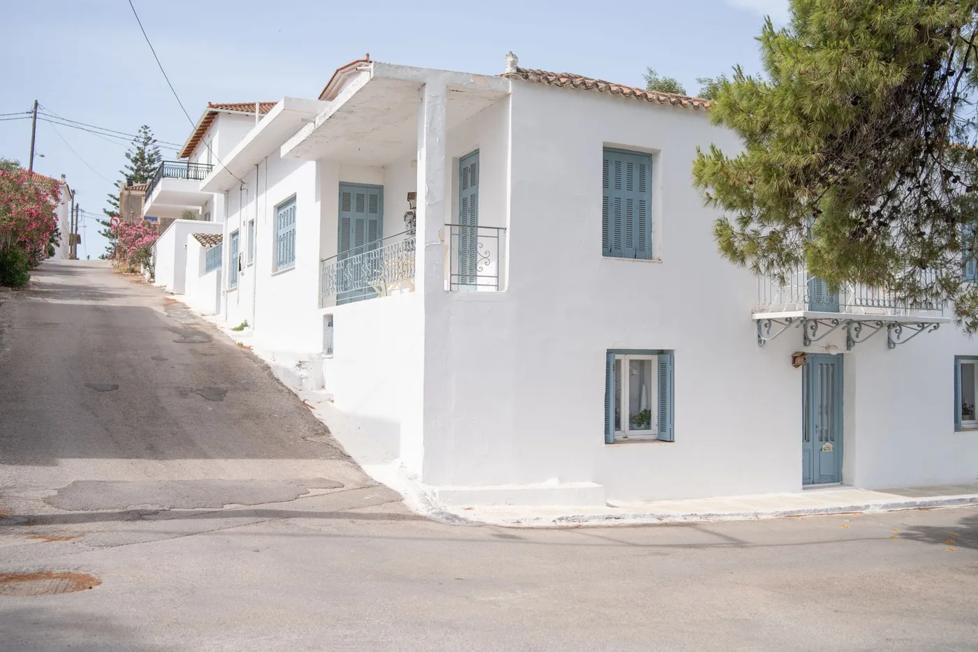 Whitewashed Greek house with blue shutters and a balcony on a quiet street corner